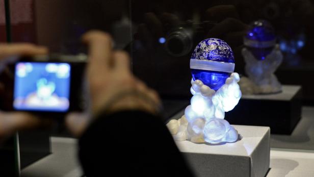 Eine Person fotografiert eine beleuchtete Skulptur mit einer blauen Kugel.