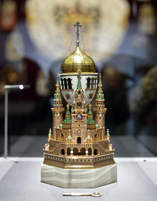 Ein Fabergé-Ei in Form einer goldenen Burg mit grünen Akzenten und einer kleinen goldenen Schlüssel liegt davor.