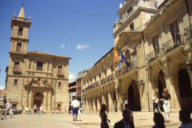 Ein belebter Platz mit historischen Gebäuden und einer Kirche in einer spanischen Stadt.