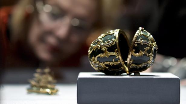 Ein geöffnetes Fabergé-Ei mit Goldverzierungen steht auf einem Sockel.
