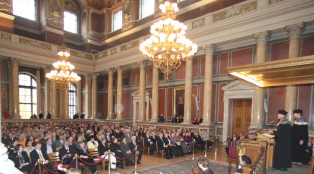 Eine große Menschenmenge in einem festlichen Saal mit Kronleuchtern und Säulen.