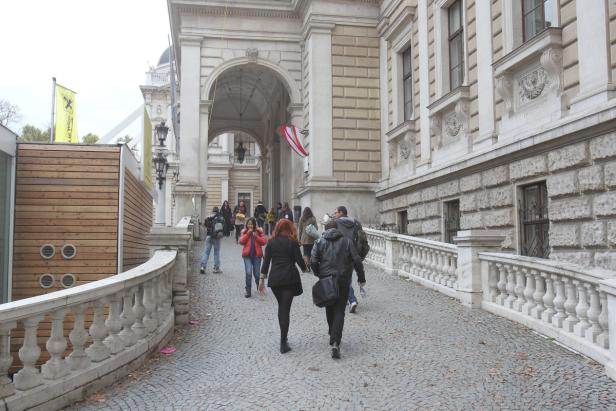 Menschen gehen auf einem gepflasterten Weg unter einem Torbogen hindurch.