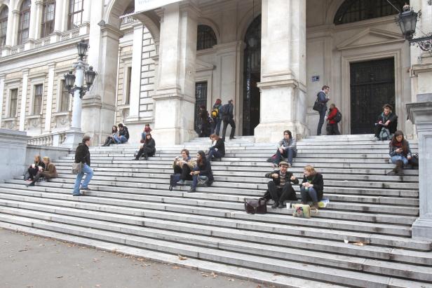 Viele Menschen sitzen auf den Stufen vor einem großen Gebäude.