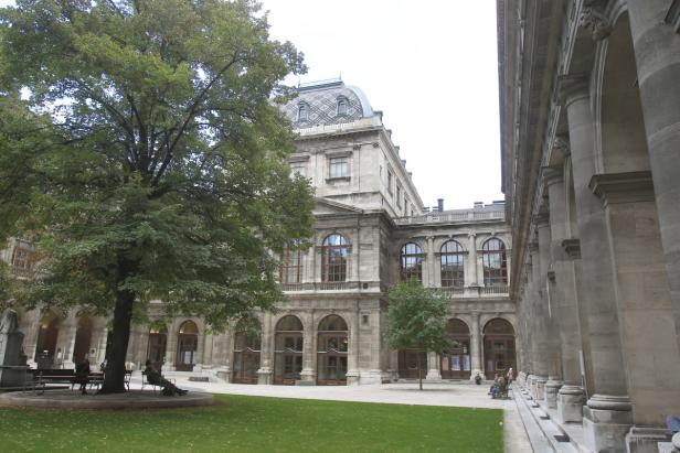 Der Arkadenhof der Universität Wien mit Bäumen und Menschen auf Bänken.