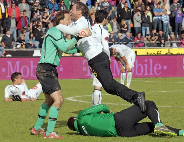 Zwei Fußballspieler umarmen sich auf dem Spielfeld, während andere am Boden liegen.