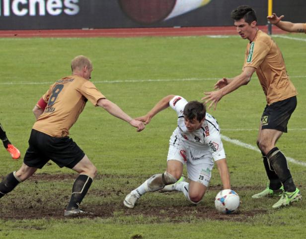 Ein Fußballspieler liegt auf dem Rasen, während zwei andere Spieler sich ihm nähern.