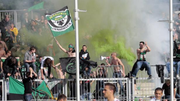 Fußballfans zünden grüne Rauchbomben und schwenken Fahnen im Stadion.