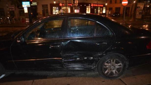 Ein schwarzes Auto mit deutlichen Unfallschäden an der Seite steht am Straßenrand.