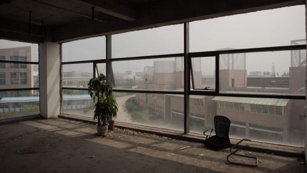 Ein leerer Raum mit einem Stuhl und einer Pflanze vor einem großen Fenster mit Blick auf eine Stadt.