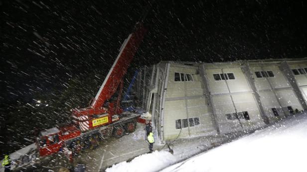 Ein Kran steht nachts im Schnee vor einem beschädigten Gebäude.