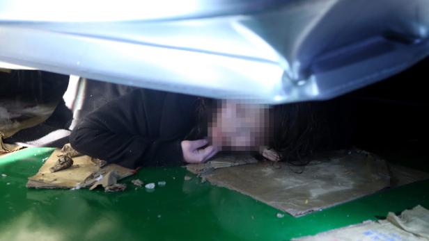 Eine Person liegt unter einem Auto auf Pappe und einer grünen Oberfläche.