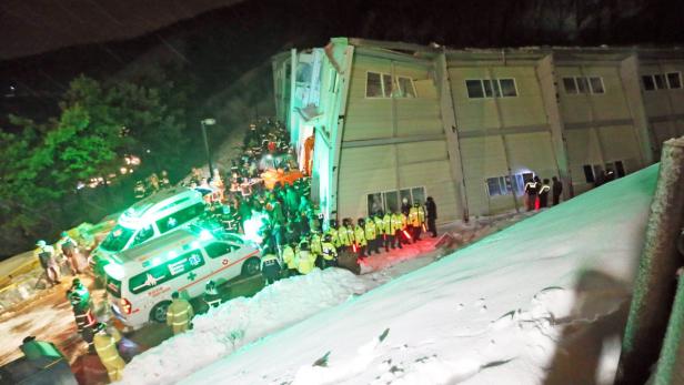 Nach einem Erdrutsch stehen Rettungskräfte und Krankenwagen vor einem beschädigten Gebäude.