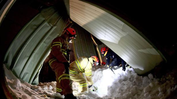 Drei Feuerwehrleute räumen Schnee von einem teilweise eingestürzten Dach.