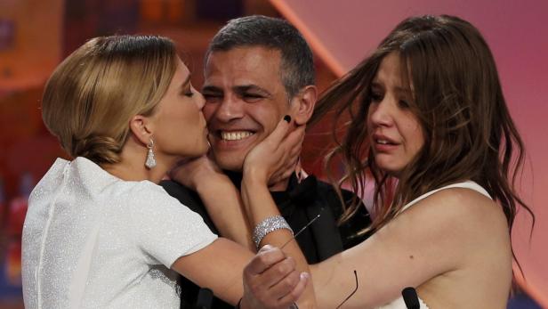 Zwei Frauen umarmen einen Mann, eine weint, die andere gibt ihm einen Kuss.