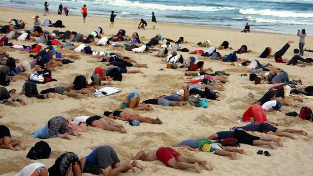 Viele Menschen liegen am Strand und machen Yogaübungen.