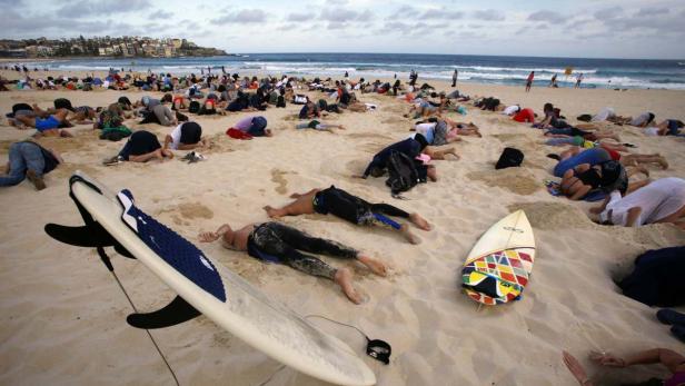 Eine Gruppe von Menschen liegt am Strand, einige mit Surfbrettern in der Nähe.