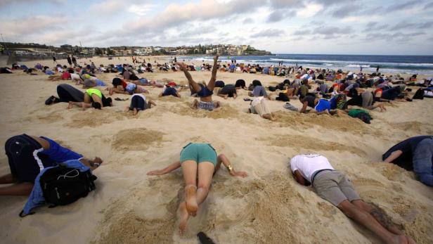 Viele Menschen liegen mit dem Gesicht nach unten am Strand.