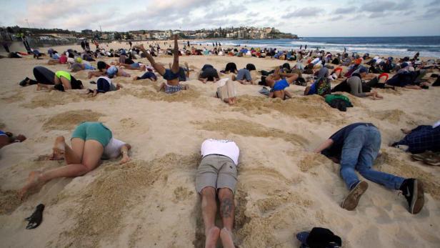 Viele Menschen stecken ihre Köpfe in den Sand am Strand.