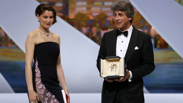 Eine Frau in Abendgarderobe und ein Mann im Smoking präsentieren die Goldene Palme von Cannes.