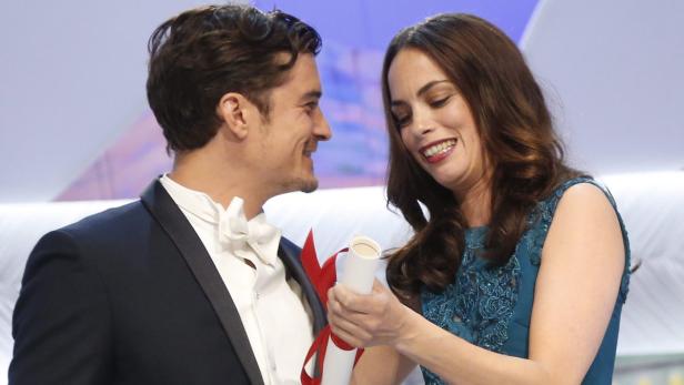 Orlando Bloom und eine Frau halten lächelnd eine Urkunde in den Händen.