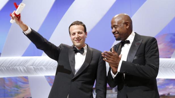 Ein Mann hält eine Urkunde in die Höhe, während ein anderer Mann ihm applaudiert.