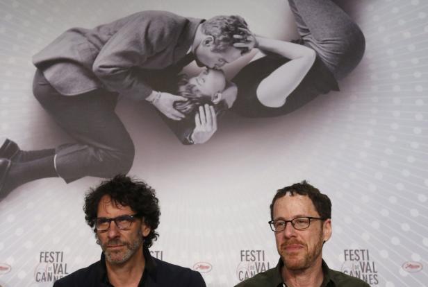 Zwei Männer sitzen vor einem Poster mit einem küssenden Paar.