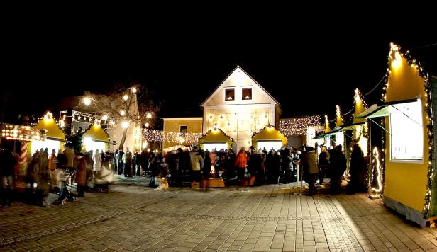 Ein belebter Weihnachtsmarkt mit Menschen und festlicher Beleuchtung bei Nacht.