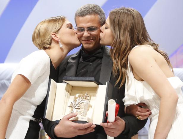 Zwei Frauen küssen einen Mann, der eine Goldene Palme hält.