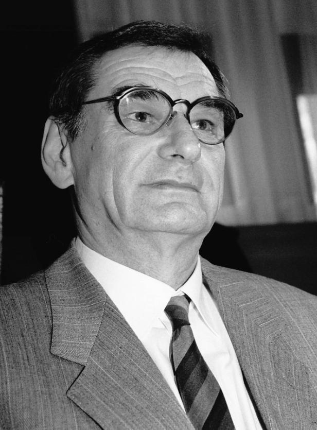 Ein Mann mit Brille, Anzug und Krawatte blickt nachdenklich zur Seite.