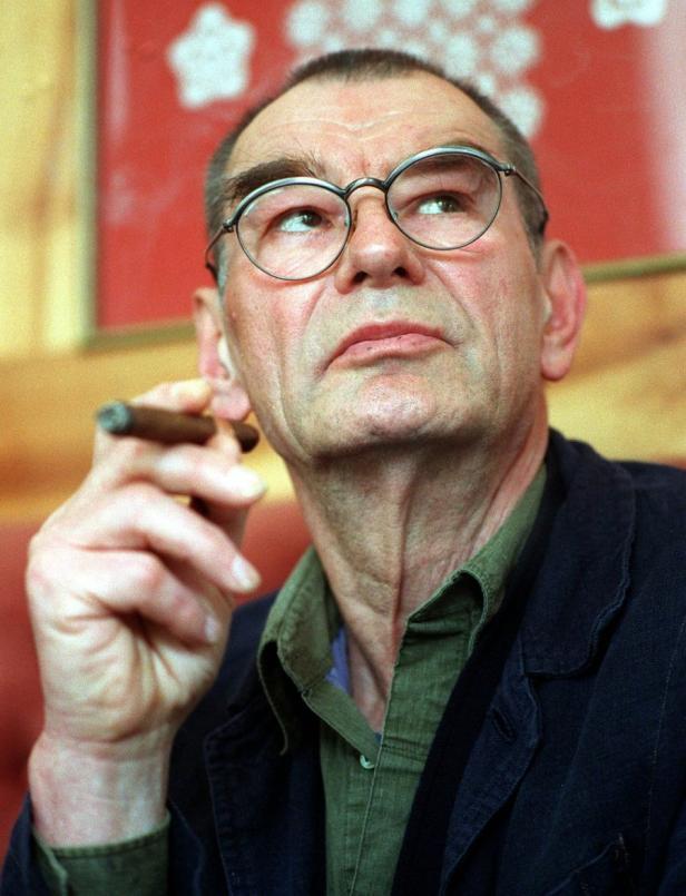 Ein Mann mit Brille und Zigarre blickt nachdenklich nach oben.