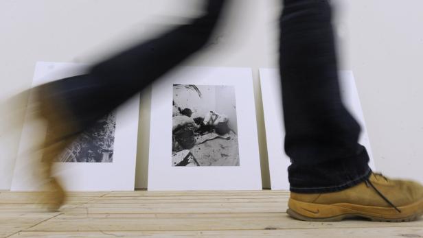 Eine Person geht an einer Kunstausstellung mit Schwarz-Weiß-Fotografien vorbei.