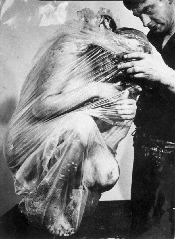 Eine Person ist in Plastikfolie eingewickelt, während eine andere Person sie berührt.