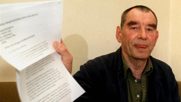 Ein Mann hält ein aufgeschlagenes Dokument in der Hand und streckt die Zunge heraus.