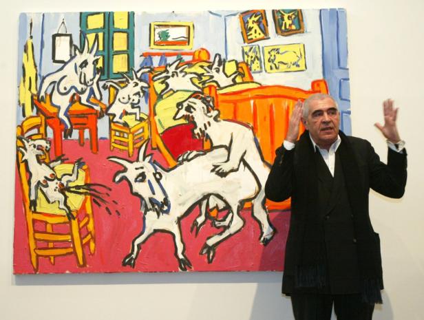 Ein Mann gestikuliert vor einem Gemälde mit Ziegen in einem Innenraum.