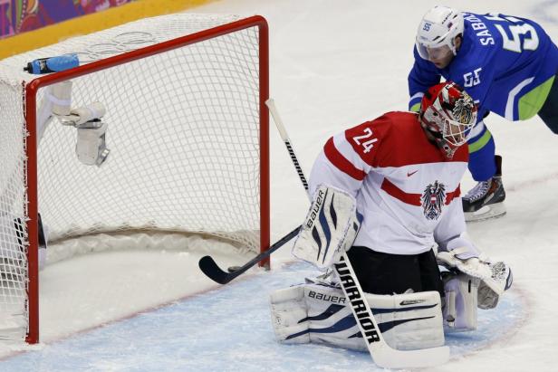 Ein österreichischer Eishockeytorwart verteidigt sein Tor gegen einen slowenischen Spieler.