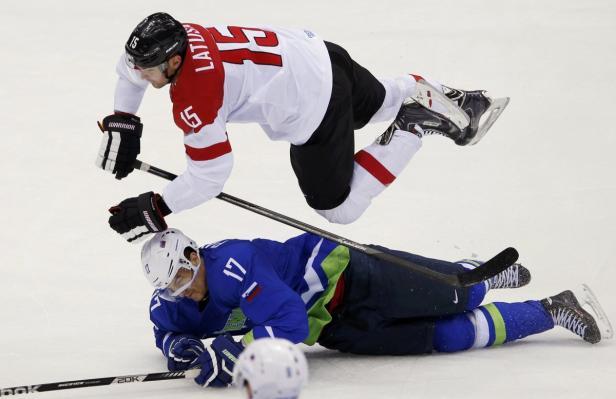 Ein Eishockeyspieler in Weiß und Rot springt über einen am Boden liegenden Spieler in Blau.