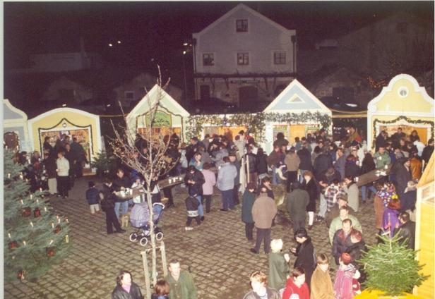 Ein belebter Weihnachtsmarkt mit Menschen vor dekorierten Hütten.