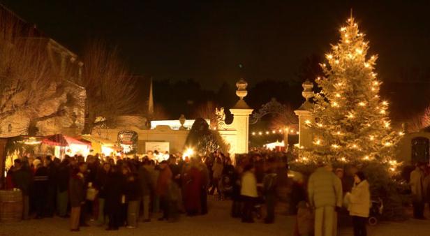 Ein Weihnachtsmarkt mit Menschenmenge und einem beleuchteten Weihnachtsbaum im Vordergrund.