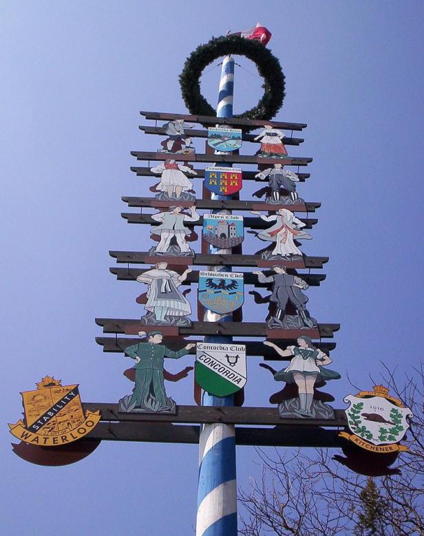 Ein Maibaum mit Wappen und Figuren verschiedener Vereine unter blauem Himmel.