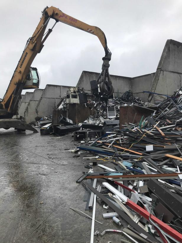 Ein Bagger mit Greifarm bewegt Schrott auf einem Recyclinghof.