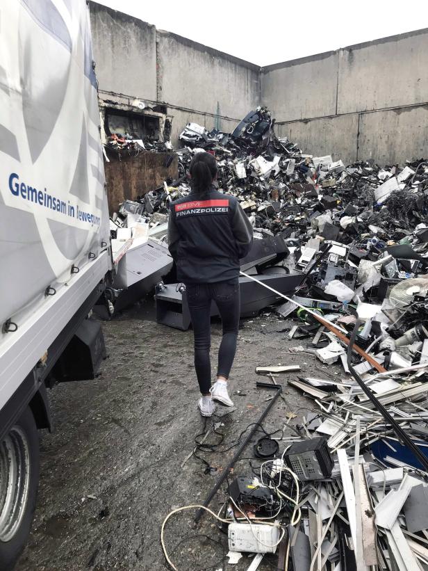 Eine Finanzpolizistin steht vor einem Container voller Elektroschrott.