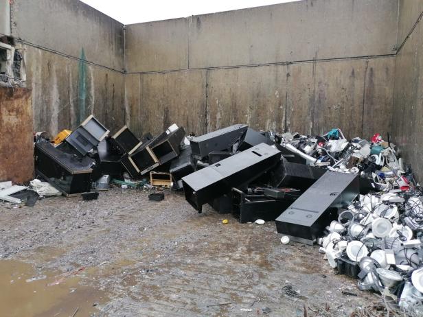 Elektroschrott, darunter Lampen und Computergehäuse, liegt in einem Container.