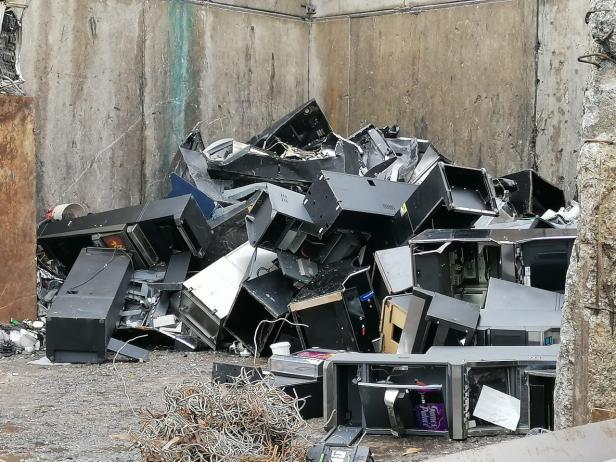 Ein Schrotthaufen aus alten Spielautomaten vor einer Betonwand.