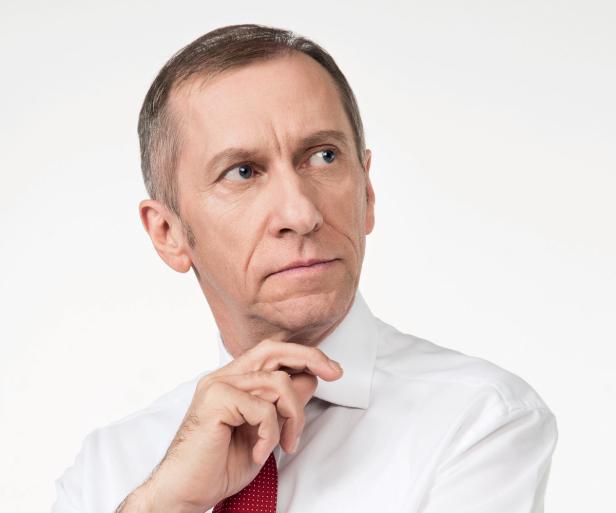 Ein nachdenklicher Mann im Hemd mit Krawatte blickt zur Seite.