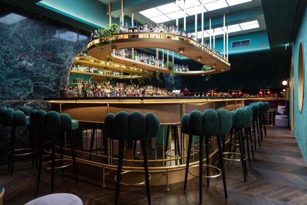 Eine Bar mit grünen Samtstühlen und einer großen Auswahl an Spirituosen hinter der Theke.
