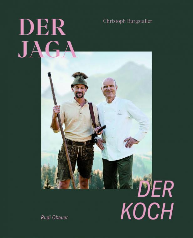 Ein Jäger in Tracht und ein Koch stehen vor einer Bergkulisse.