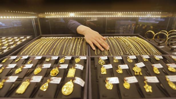 Eine Hand greift nach einer goldenen Halskette in einem Schmuckgeschäft.