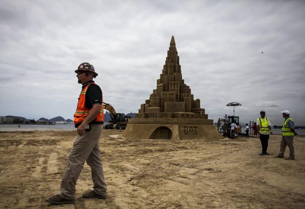 Ein Bauarbeiter geht an einer großen Sandburg mit dem CAT-Logo vorbei.
