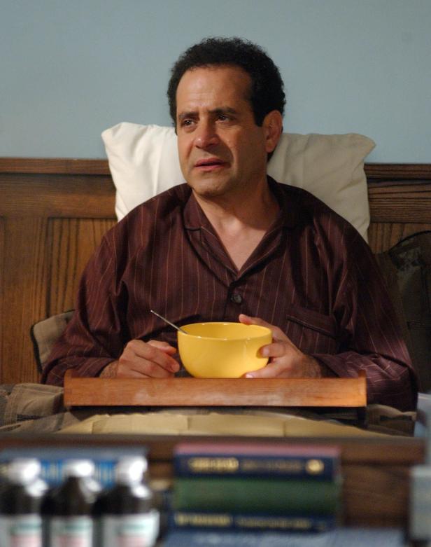 Ein Mann im Schlafanzug sitzt mit einer gelben Schüssel im Bett.