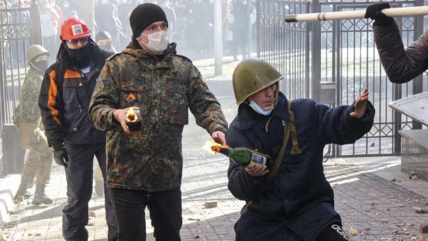 Mehrere Personen mit Molotowcocktails vor einem Gitter.